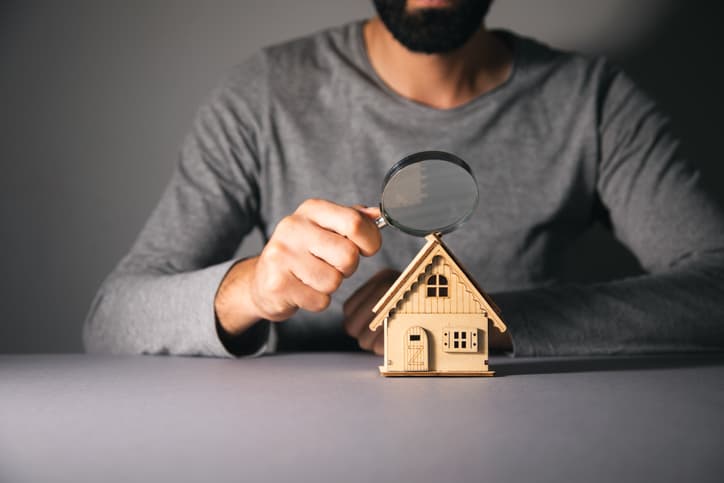 Homem investigando miniatura de casa com lupa